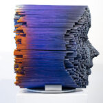 Rostos meditativos emergem das varas de madeira escalonadas nas esculturas do artista Gil Bruvel